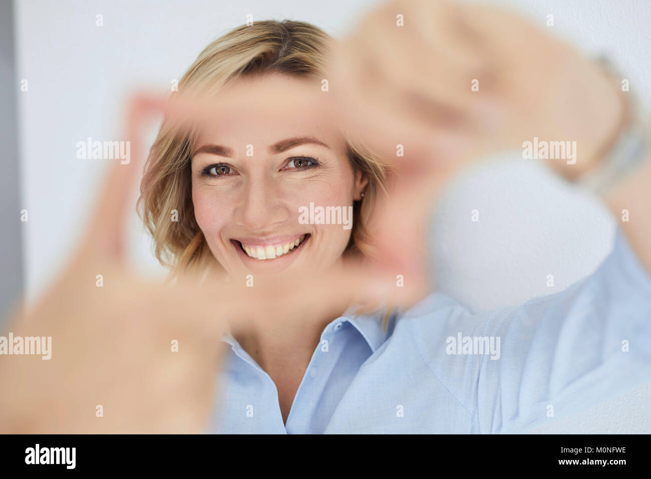 Portrait of smiling blond woman building frame with her fingers while looking at viewer Stock Photo