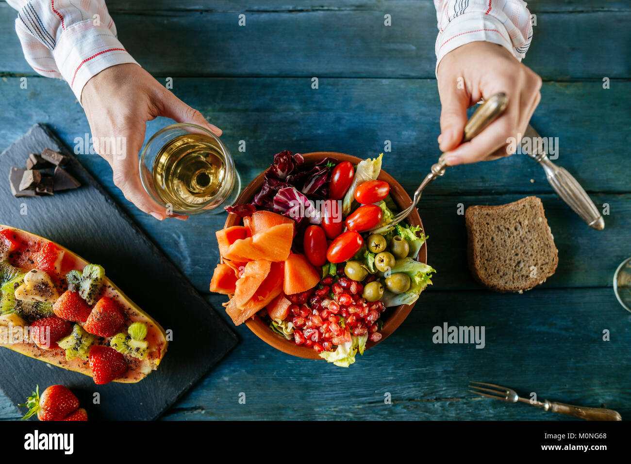 Close-up of woman's hands eating salad wit tomato, pomegranate, papaya and olives, papaya with fruits and with wine glass Stock Photo