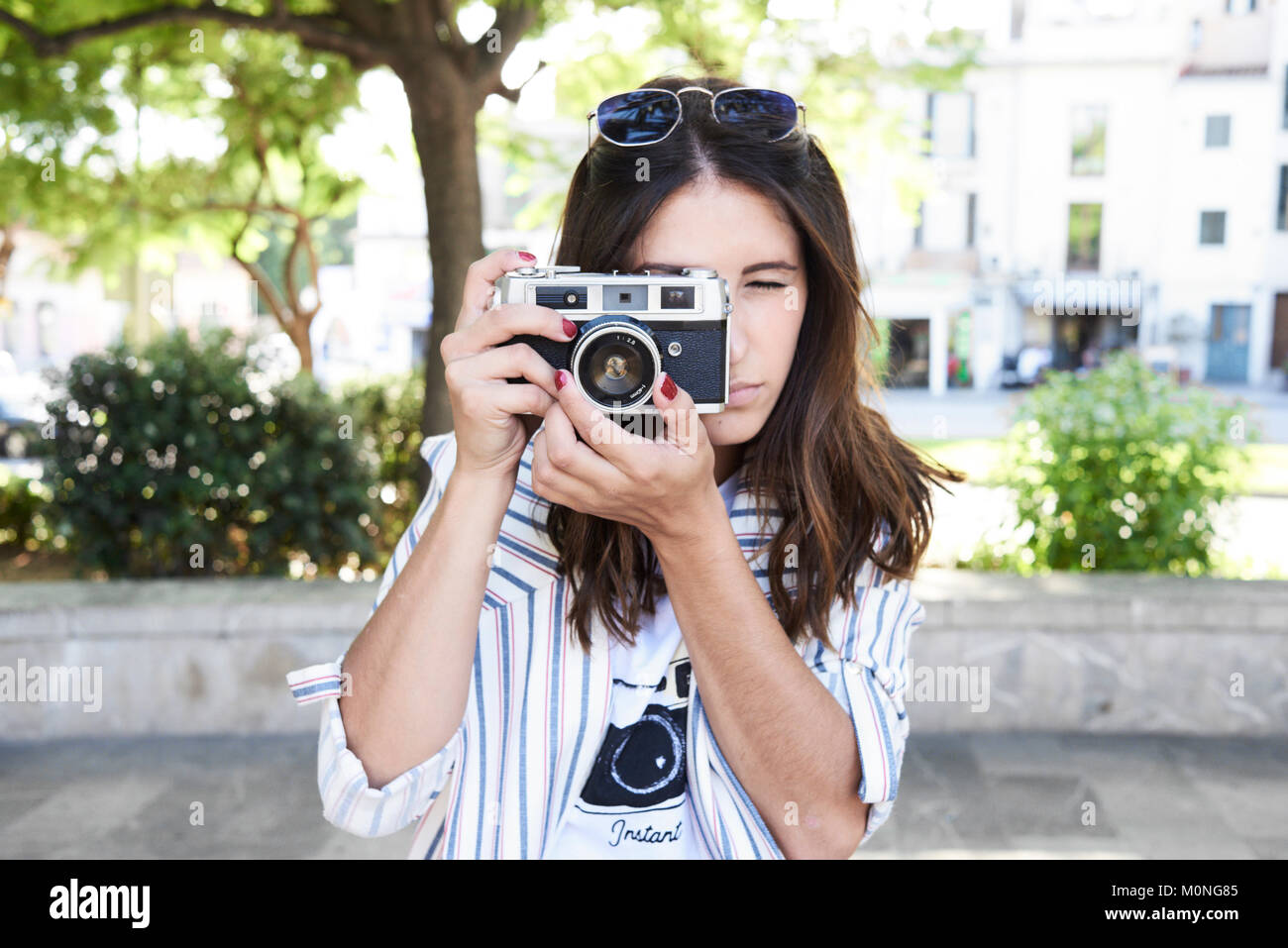 Trendy brunette photographer taking a picture with her film camera outdoors in summer. Stock Photo