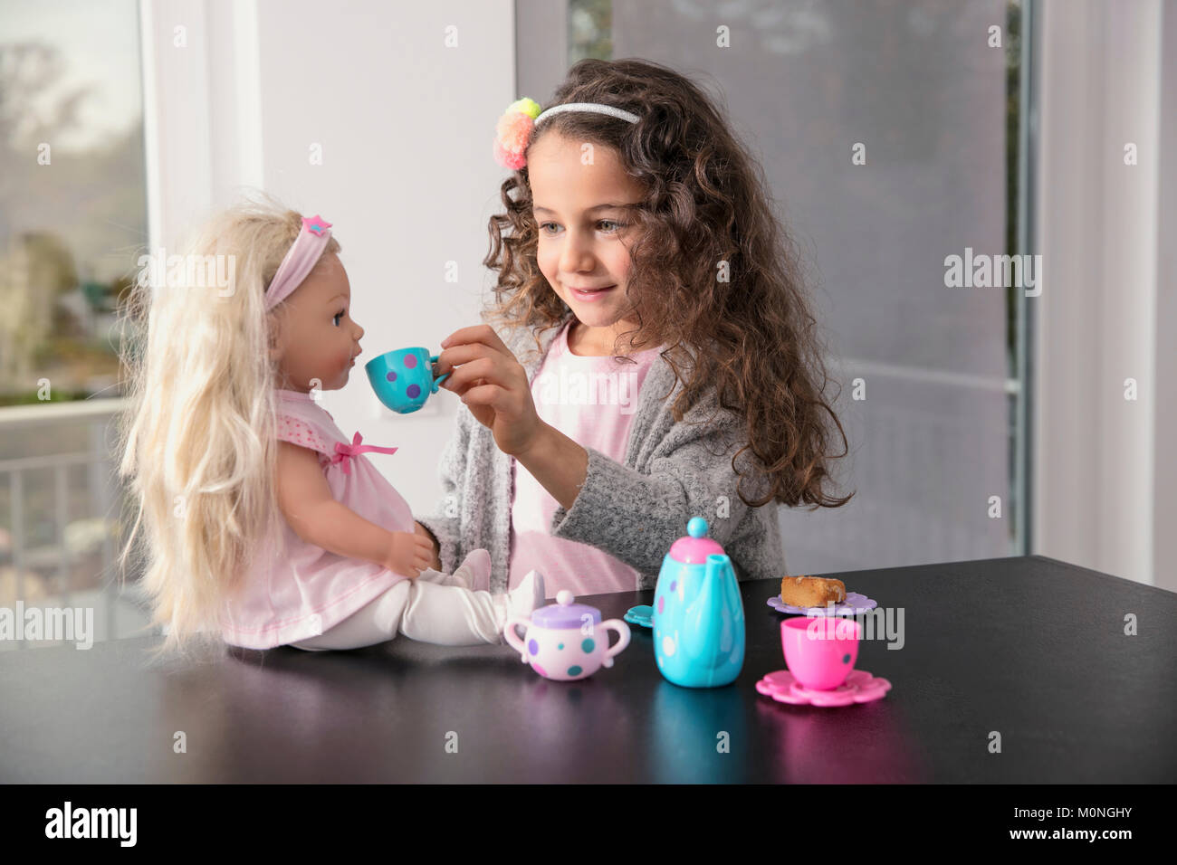 Portrait of smiling little girl playing with doll and doll's china set Stock Photo