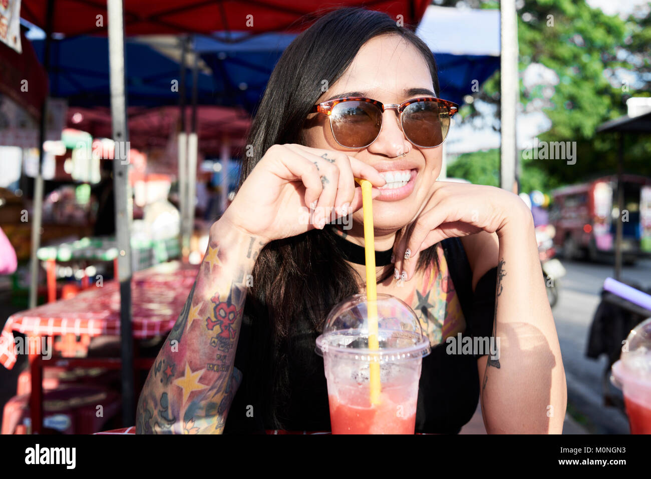 Happy asian girl drinking a smoothie while catching up with friends in summer. Stock Photo
