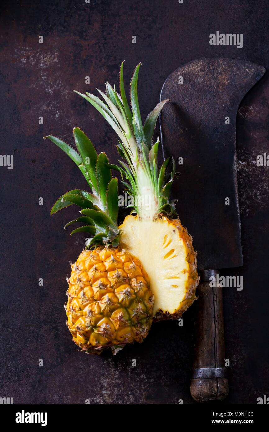 Sliced baby pineapple and old cleaver on rusty metal Stock Photo