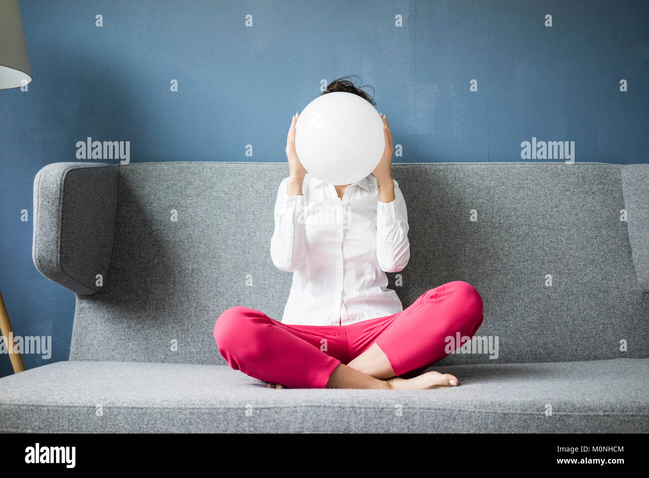 Woman sitting on couch hiding her face behind a white sphere Stock Photo