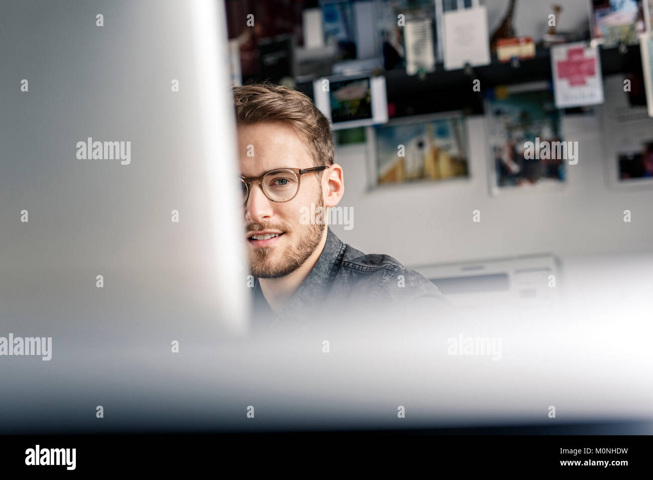 Portrait of young man behind computer screen at desk at home Stock