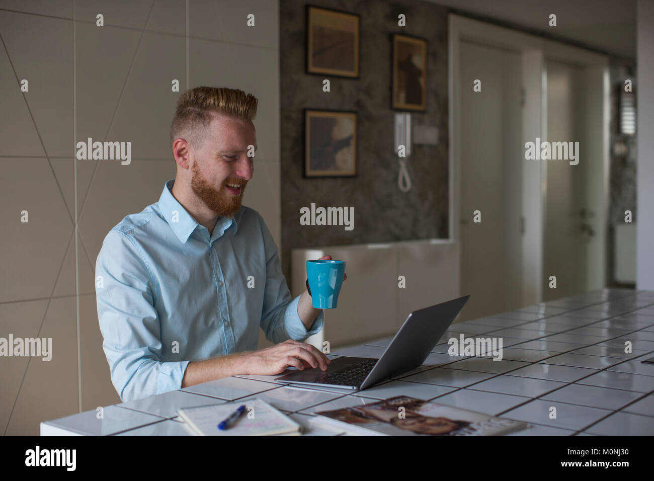 Laughing businessman with coffee mug working on his laptop at home ...