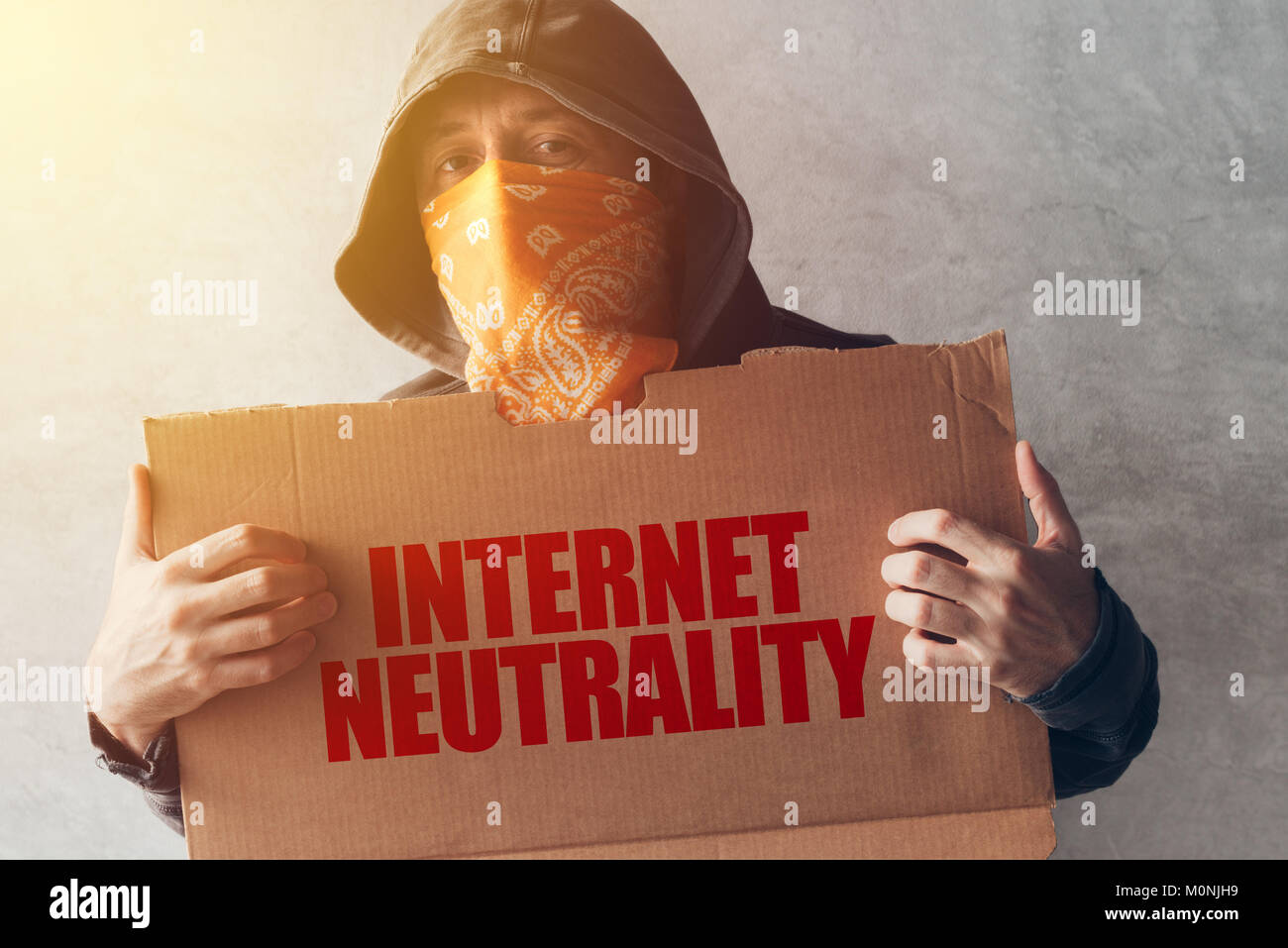 Hooded activist protestor holding Internet neutrality protest sign. Man with hoodie and scarf over face taking part in activism and fighting for the c Stock Photo