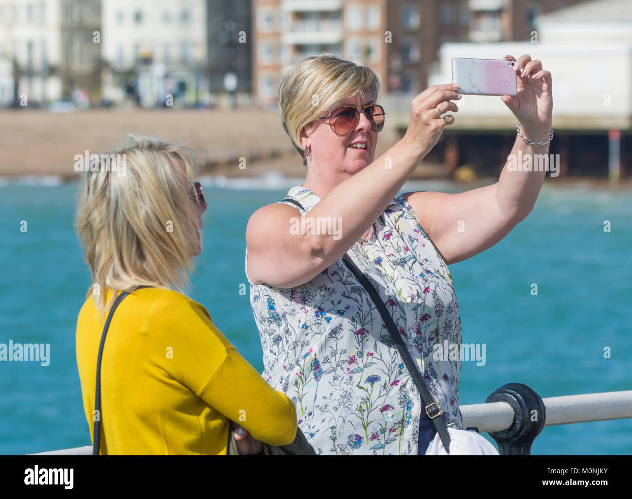 A couple of female friends at the seaside taking selfies on a smartphone in the UK. Stock Photo