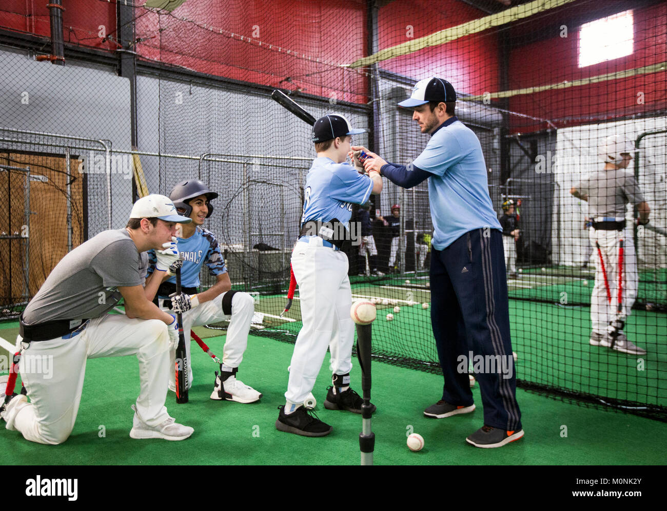Baseball coach demonstrating proper hitting technique at an indoor