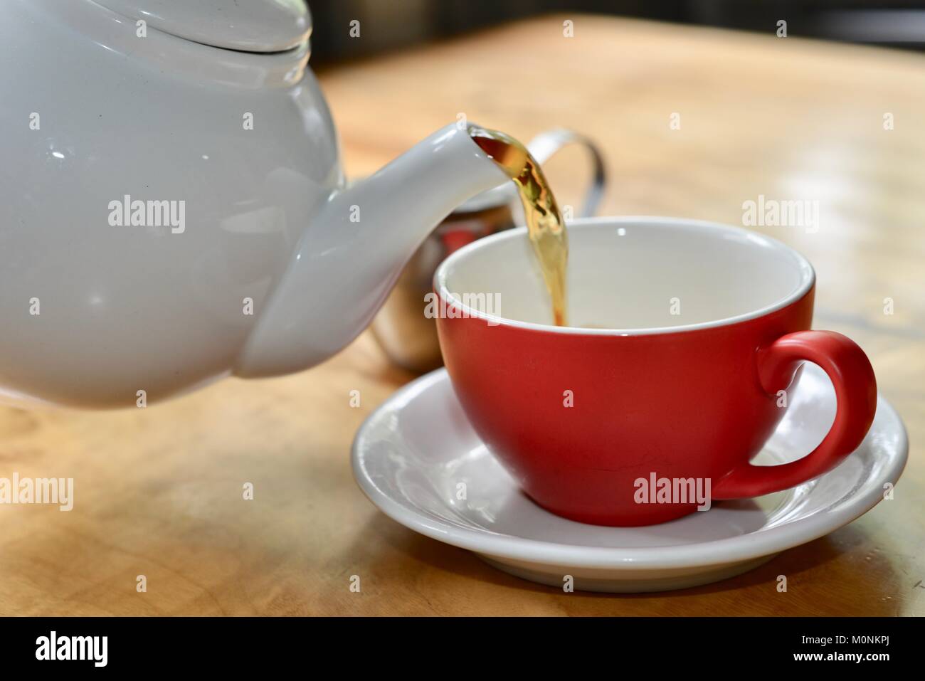 Black Tea being poured white ceramic teapot into a red cup with white