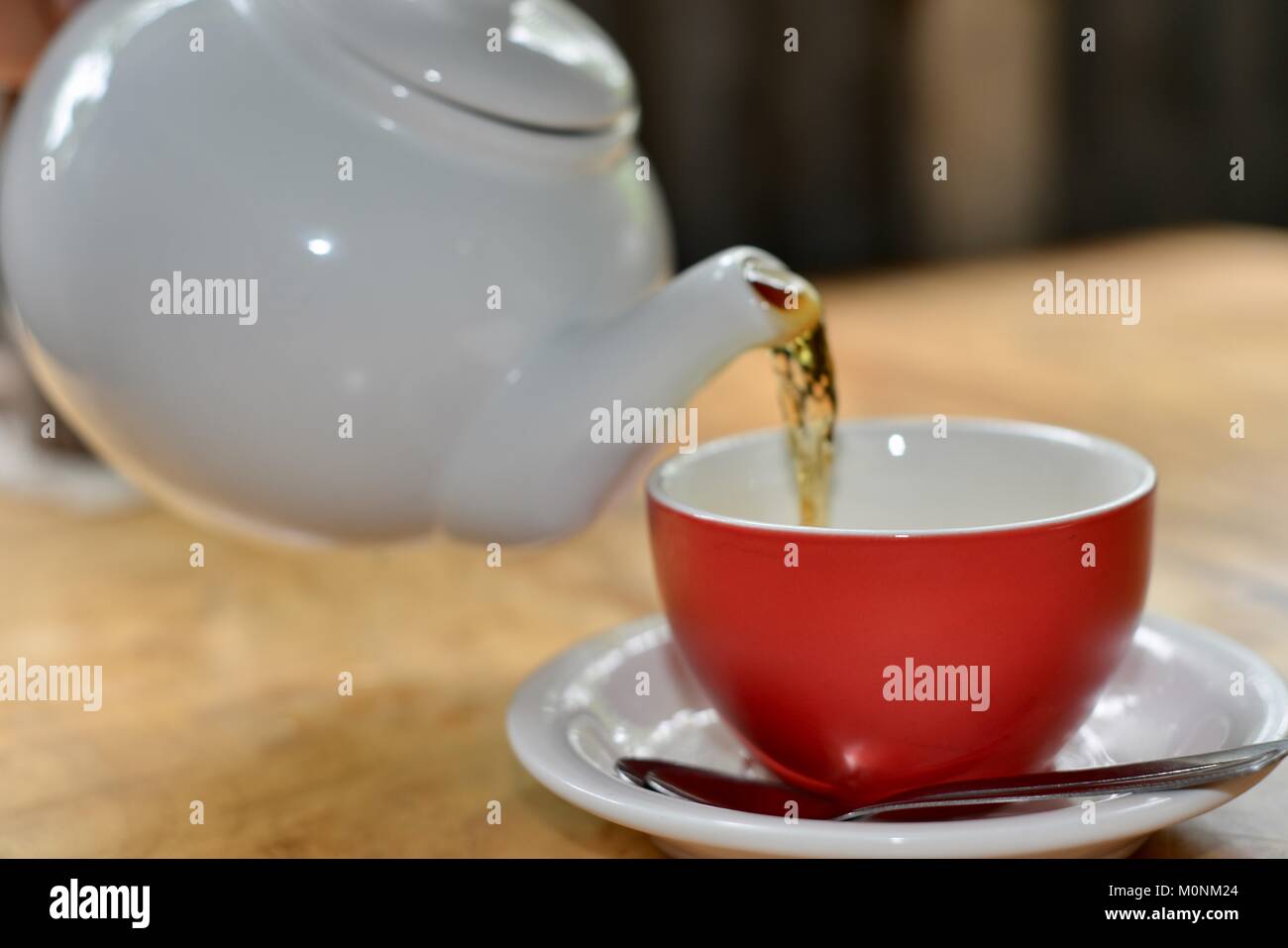 Black Tea being poured white ceramic teapot into a red cup with white