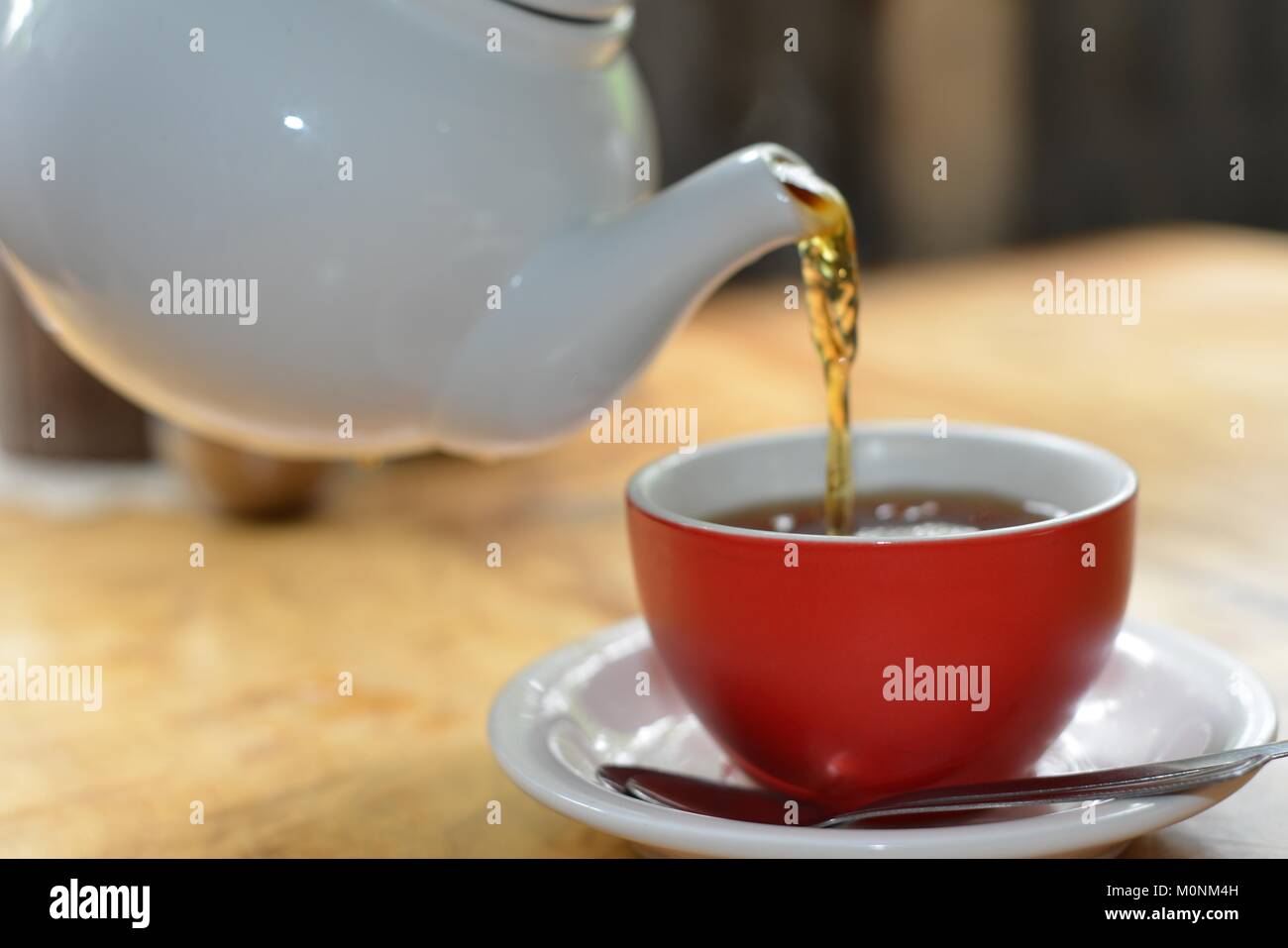 Black Tea being poured white ceramic teapot into a red cup with white