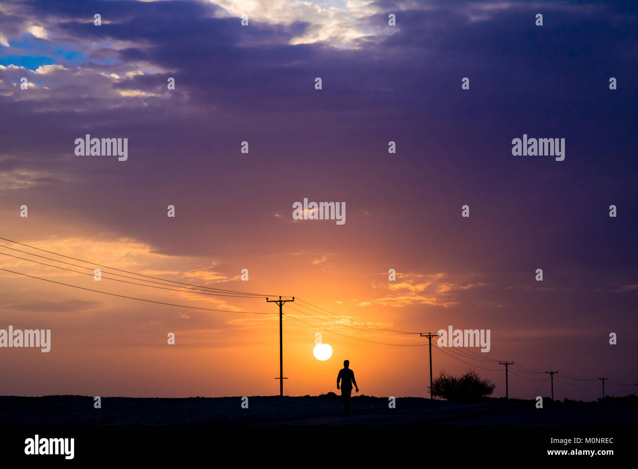 a silhouette of a man walking up a road against a sunset background ...