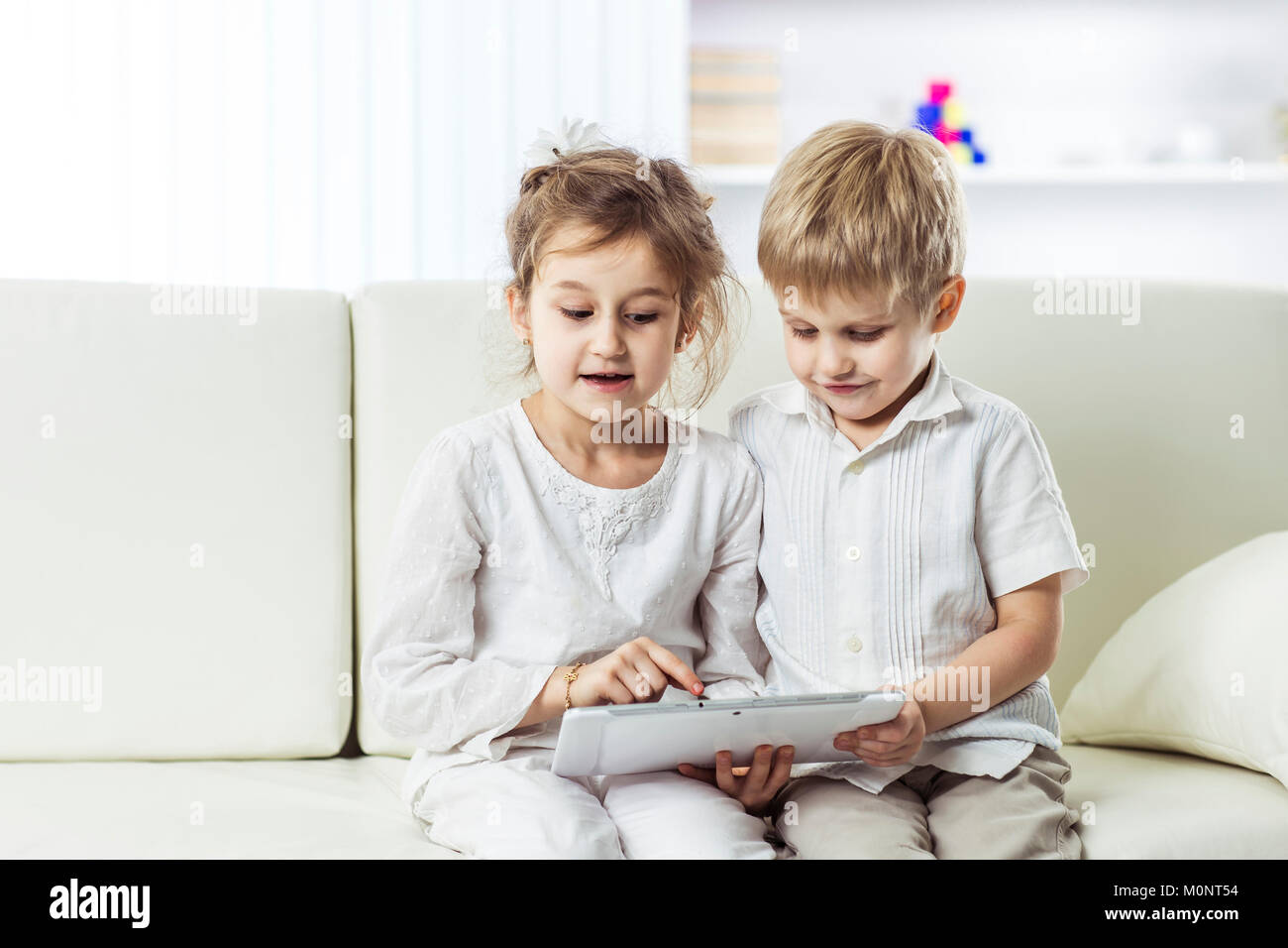 little brother and sister with digital tablet sitting on the sofa in ...