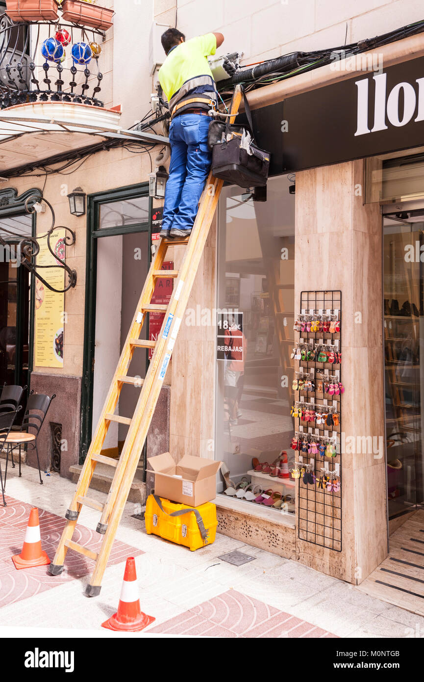 A man working up a ladder in Mahon , Menorca , Balearic Islands , Spain Stock Photo
