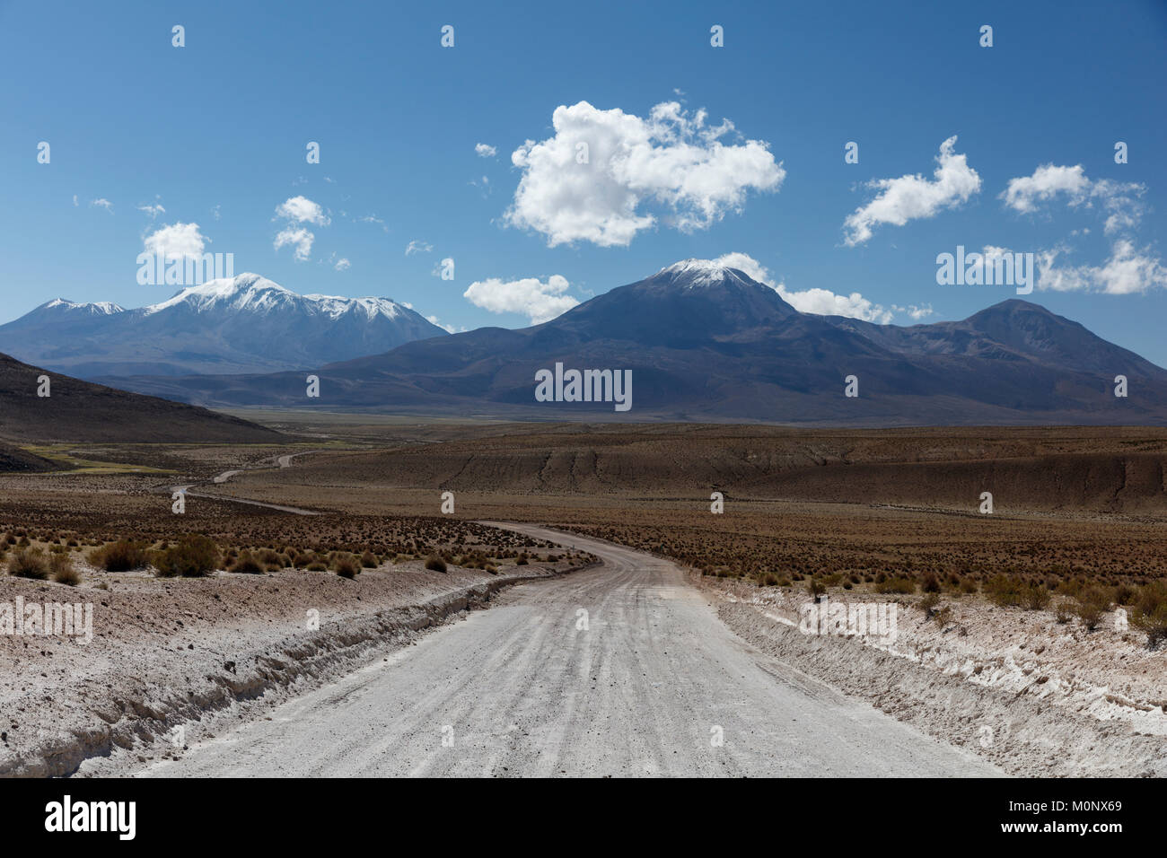 Gravel road leads through Altiplano,behind snow covered volcanoes,near Colchane,Tarapaca,Chile Stock Photo