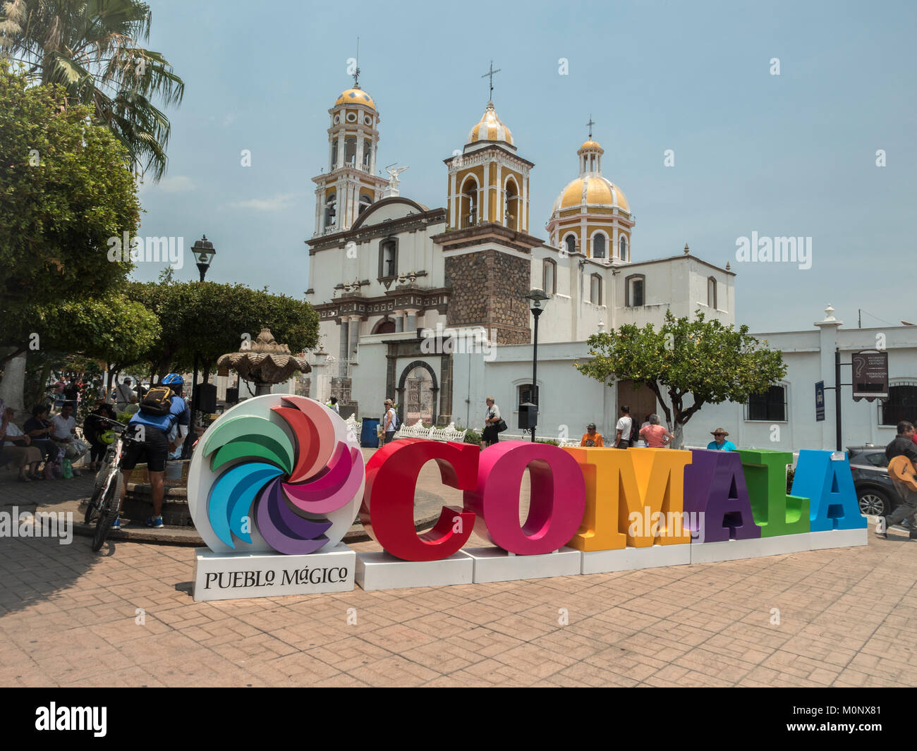 Tourists Pose In Front Of The Colourful Sign Comala A Pueblo Magico The Church of Noguerasâˆ’Iglesia de Nogueras In The Background Colima Mexico Stock Photo