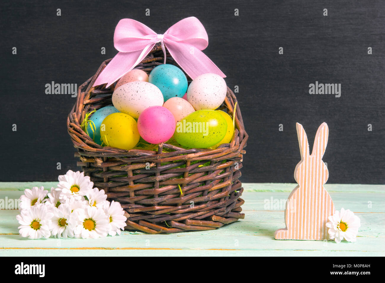 Wicker basket full of multicolored Easter eggs and a pink bow ...
