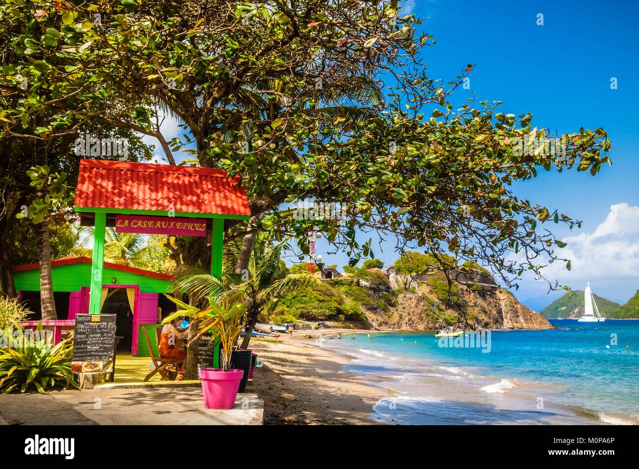 France,Caribbean,Lesser Antilles,Guadeloupe,Les Saintes,Terre-de-Haut,shady restaurant terrace La Case aux Epices at Anse Fond Curé,the battery of the Tête-Rouge in the background recalls the stormy past between French and British in the region Stock Photo