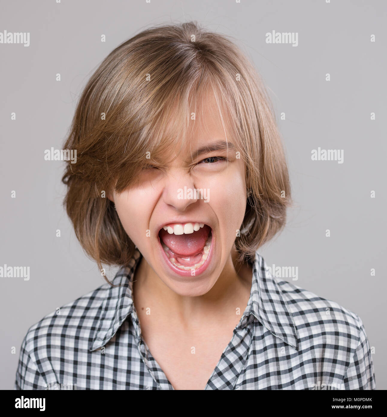 Close-up emotional portrait of attractive angry child teenager girl screaming wide open mouth. Funny cute child on gray background. Negative human fac Stock Photo