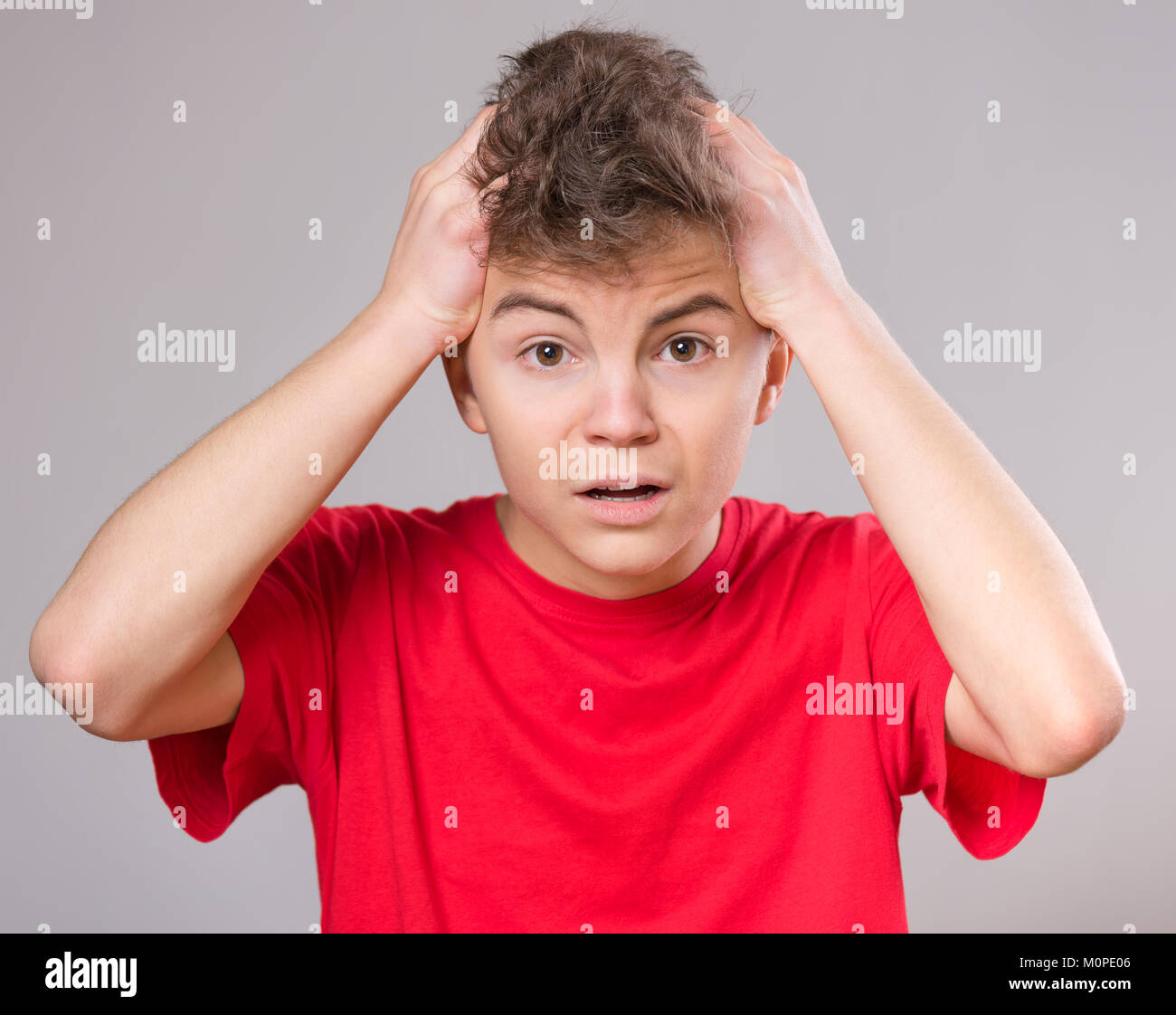 Emotional portrait of excited teen boy. Funny cute surprised child 14 year old with mouth open in amazement. Shocked teenager with hands on head, on g Stock Photo