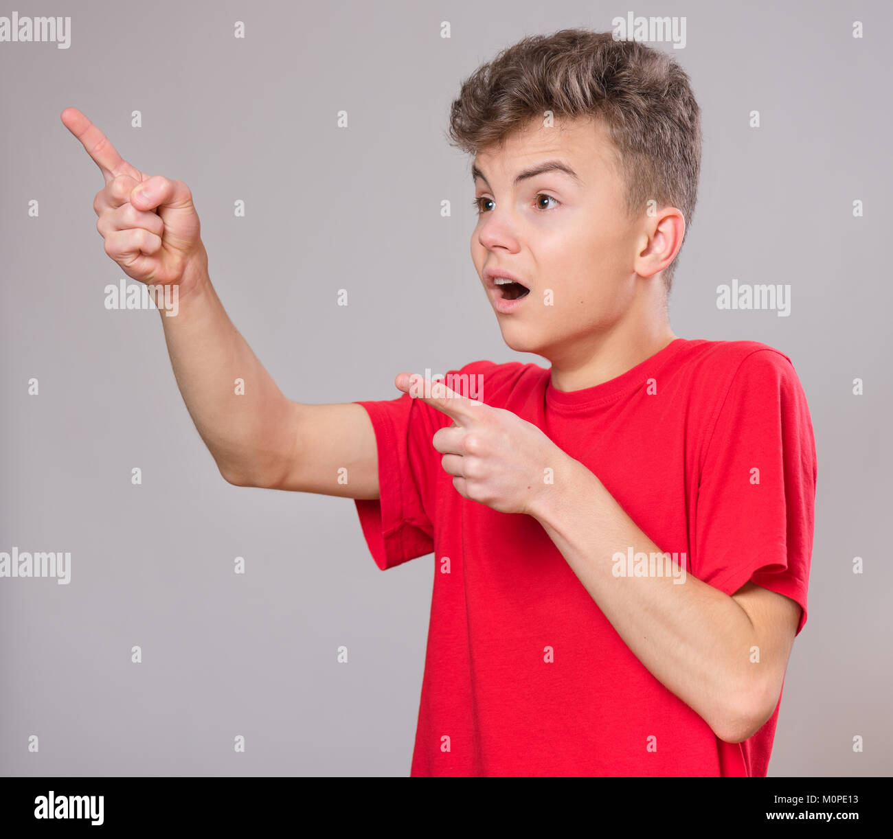Emotional portrait of excited teen boy. Funny cute surprised child 14 year old with mouth open in amazement. Shocked teenager pointing fingers up, on  Stock Photo