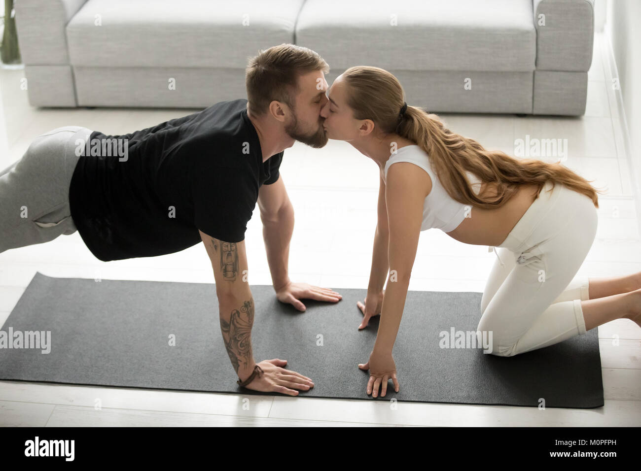 Sporty fit man performing plank exercise at home kissing woman Stock Photo