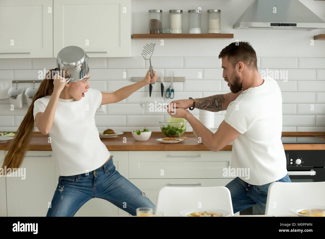 Funny couple having fun fighting with kitchen utensils cooking t Stock Photo