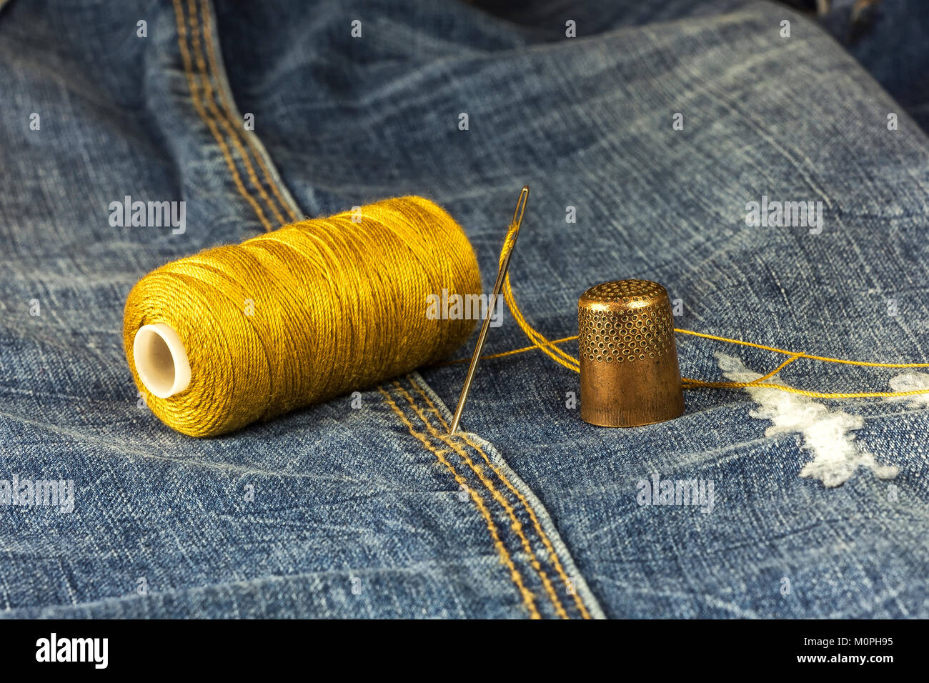 On denim is a spool of thread, needle and thimble Stock Photo
