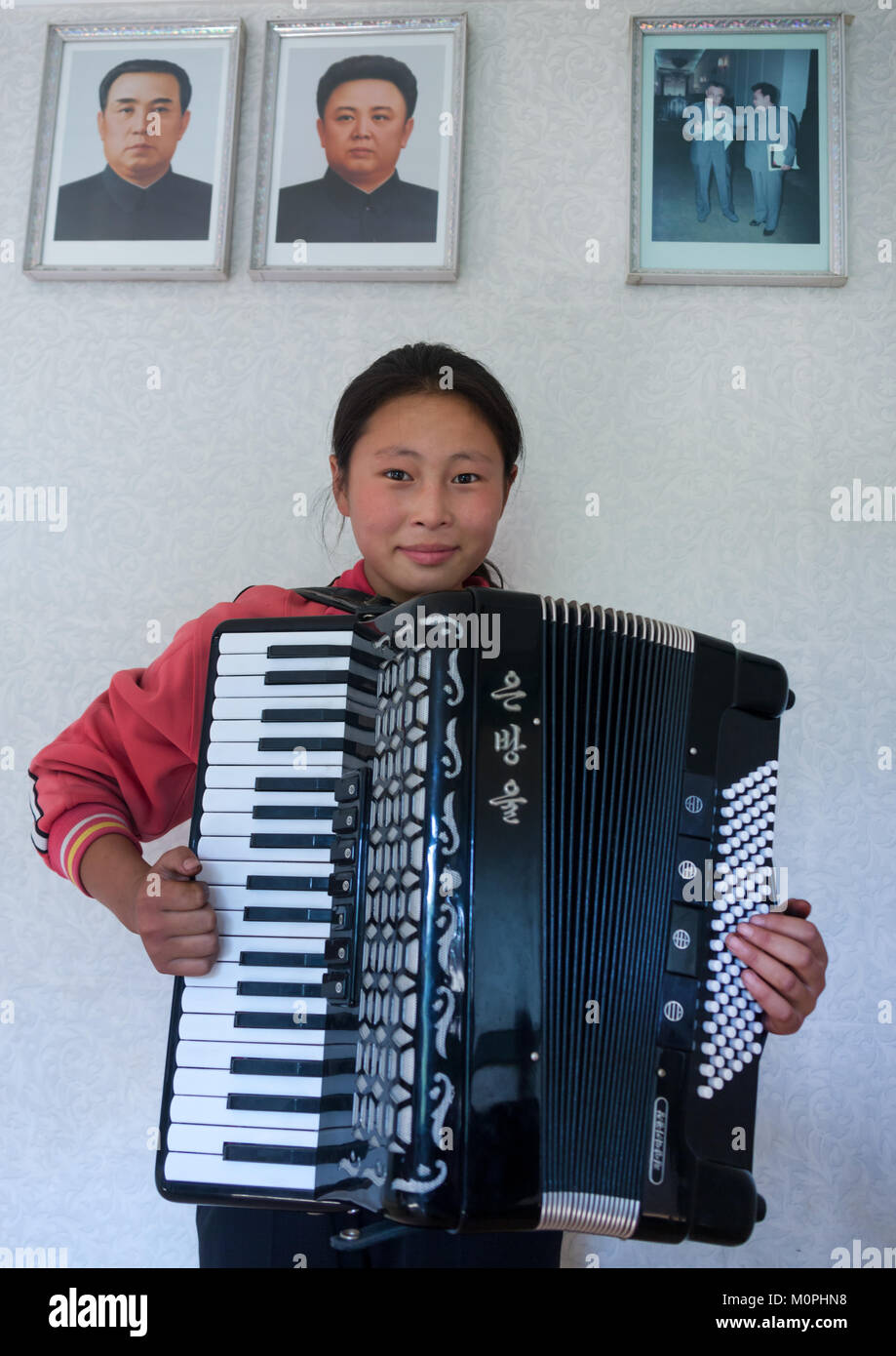 North Korean girl playing accordion under the Dear Leaders portaits