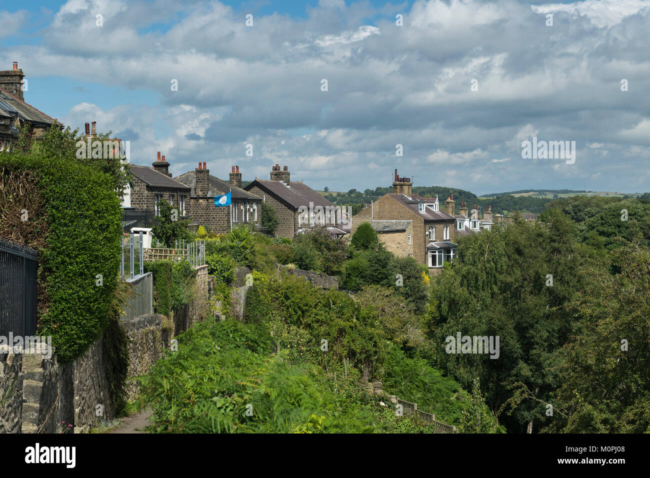 View under blue sky along row of stone houses (semis) situated at top of Baildon Bank, a steep wooded cliff - Shipley, West Yorkshire, England, UK. Stock Photo