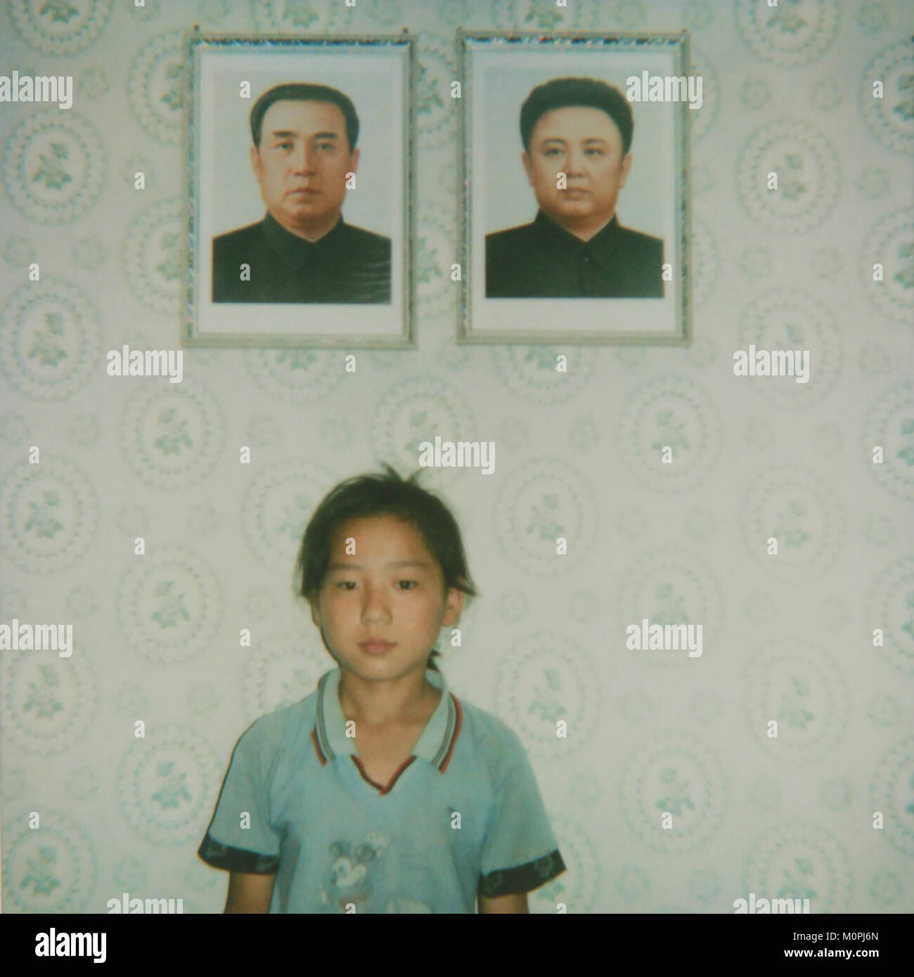 North Korean girl posing below the portraits of the Dear Leaders inside her home, South Pyongan Province, Chonsam Cooperative Farm, North Korea Stock Photo