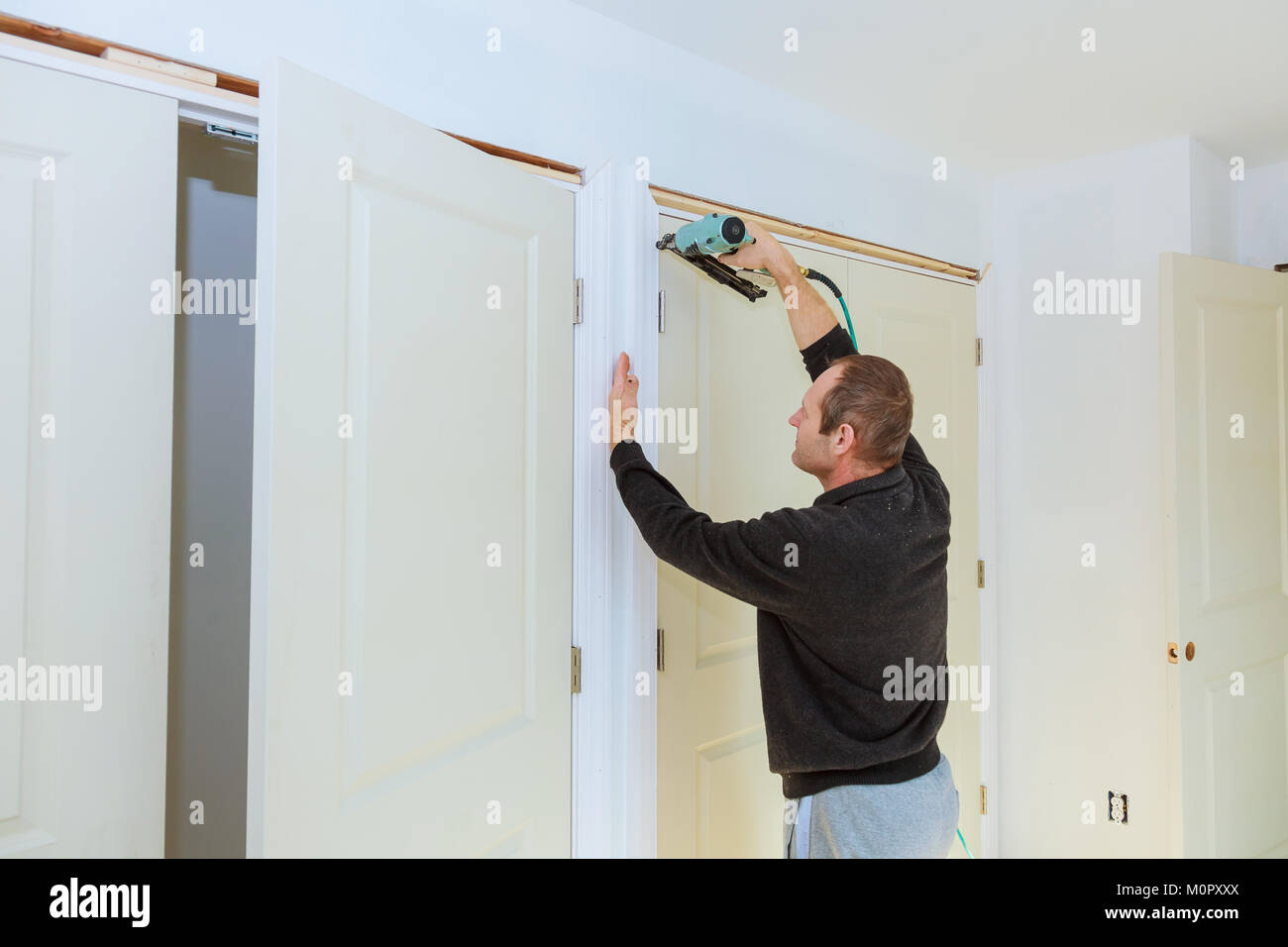 Carpenter brad using nail gun to moldings on doors, framing trim, with