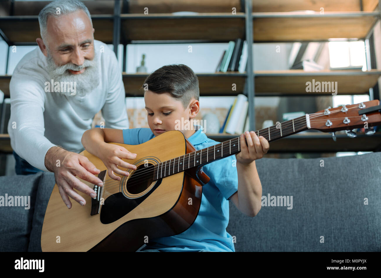 Mindful senior gentleman teaching grandson playing guitar Stock Photo