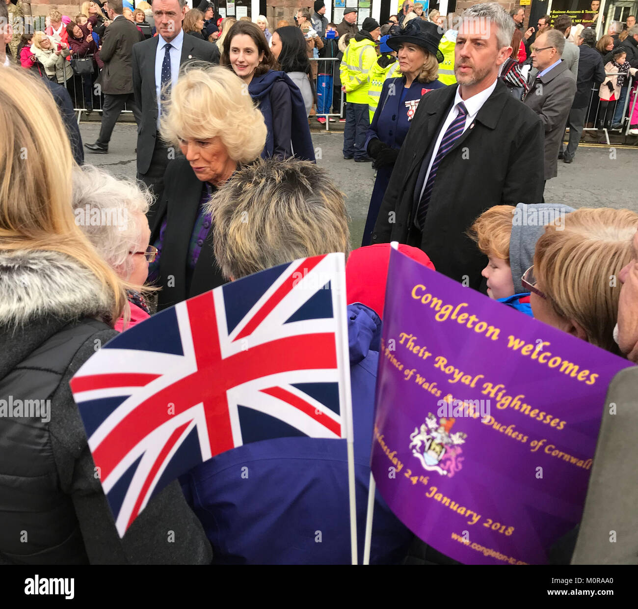 Congleton, Cheshire, England, UK. 25th January 2018. Camilla, Duchess of Cornwall greets well-wishers in Congleton Town Centre (Cheshire UK), as crowds wave commemorative flags bearing an upside-down Union Jack - a symbol of distress.  The Royal couple were visiting the Cheshire market town to visit community projects, celebrate 700 years having a Mayor and unveil sculptor Amy Goodman's statue commemorating Treo, an explosives sniffer dog, who served in Afghanistan.  After crossing the road to visit the Prince of Wales pub, couple chatted and shook hands with visitors. Stock Photo