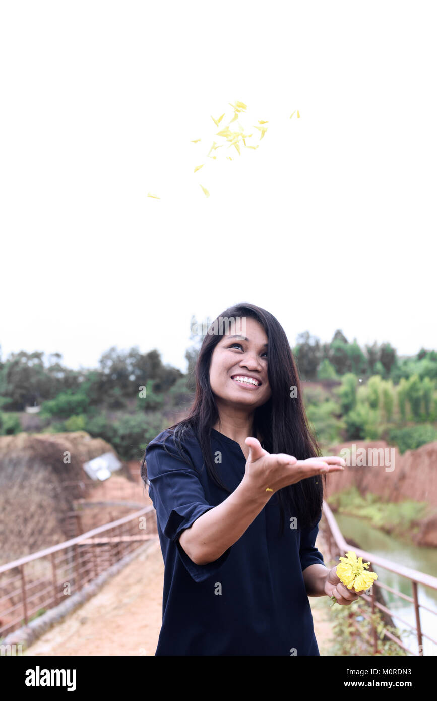 Happy Asian woman throwing flowers up in the sky surrounded by nature. Stock Photo