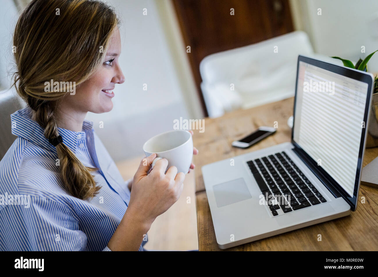 Smiling woman sitting at desk with cup of coffee and laptop Stock Photo ...