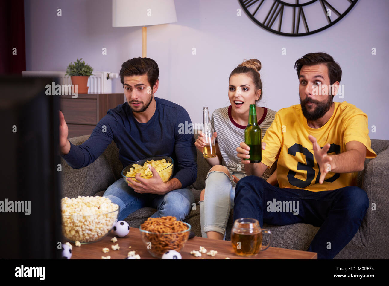 Excited friends sitting on the sofa watching Tv Stock Photo