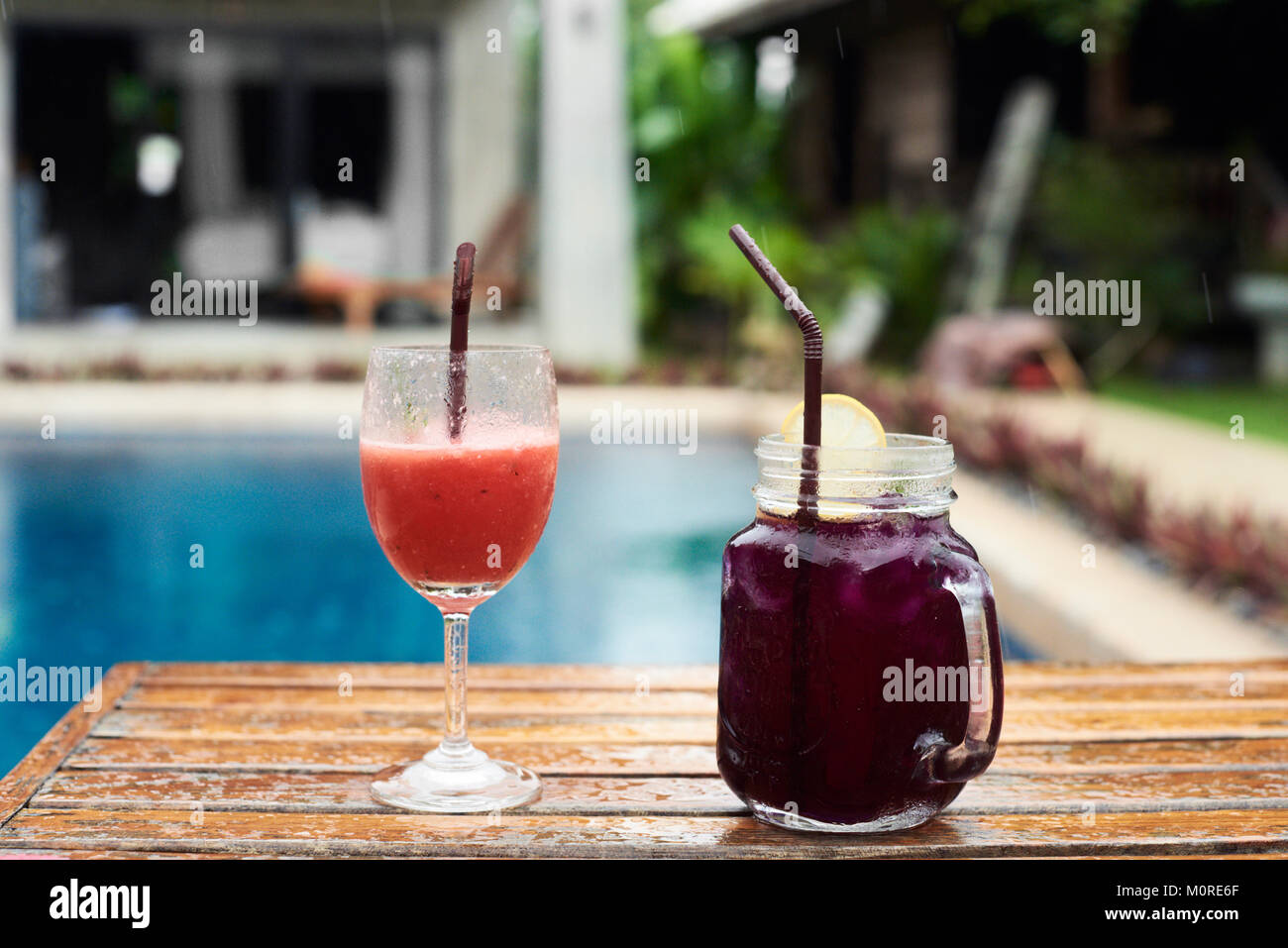 Close up of two colorful cocktails wet on a wooden hammock against swimming pool. Raining. Stock Photo