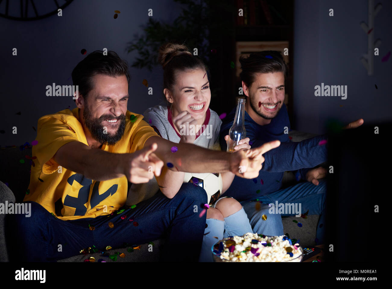 Excited friends sitting on the sofa watching Tv Stock Photo