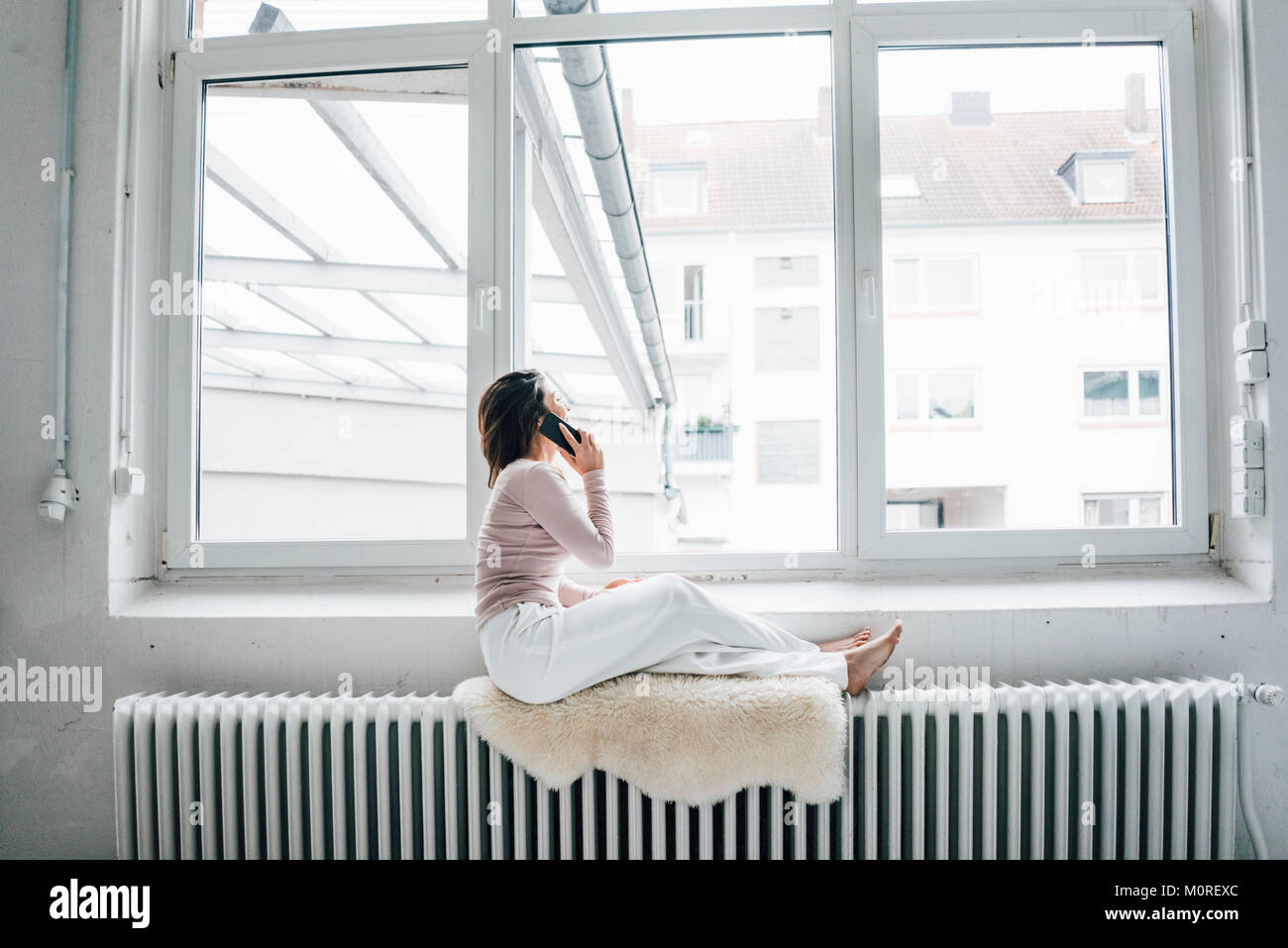 Young woman on the phone sitting on sheepskin on heater in a loft looking  out of window Stock Photo - Alamy
