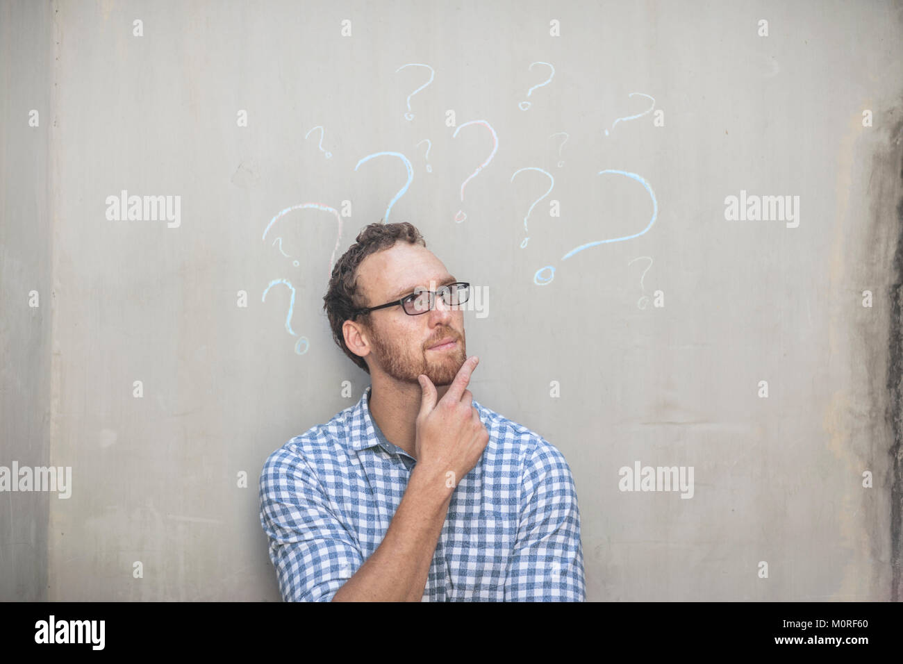 Man standing next to a concrete wall with chalk question mark drawings Stock Photo