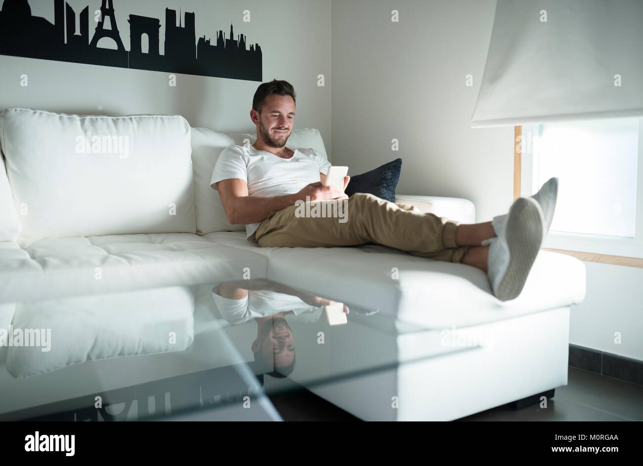 Smiling young man relaxing at home with his smartphone Stock Photo