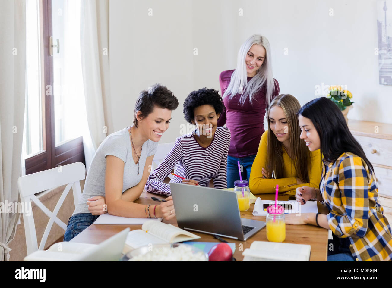 Group of female students sharing laptop at table at home Stock Photo ...