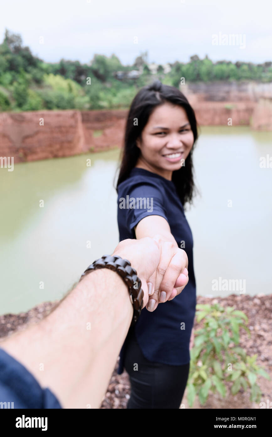 Pretty asian woman holding hand of her partner inviting to go and explore together. Stock Photo