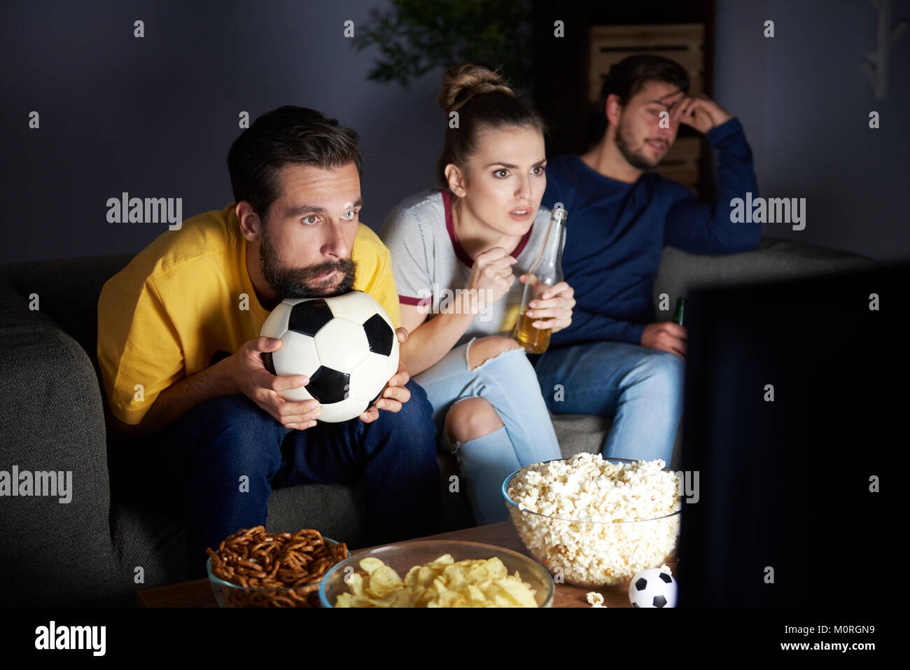 Worried friends sitting on the sofa watching Tv Stock Photo