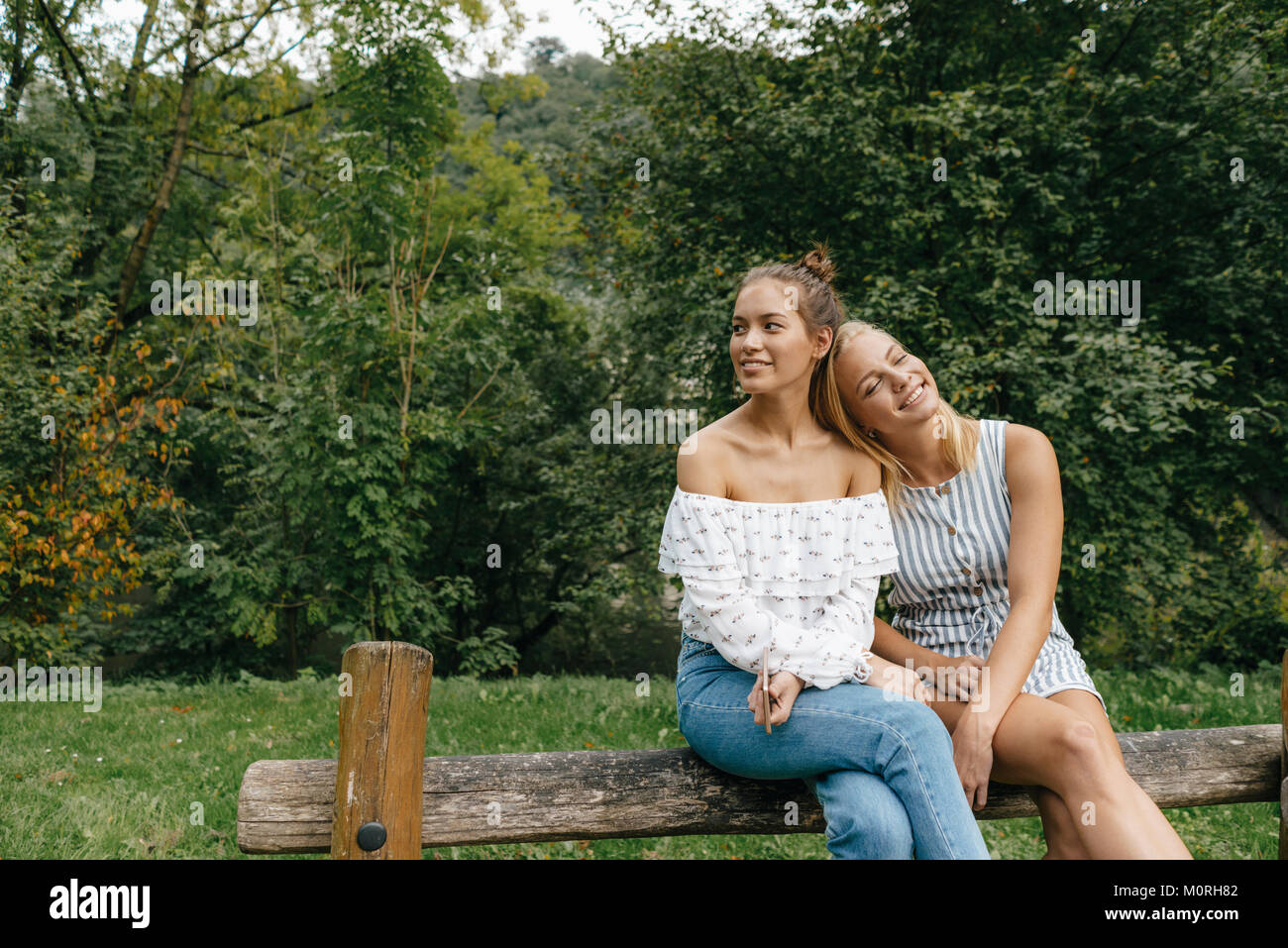 Two happy young women sitting on fence in a park Stock Photo - Alamy