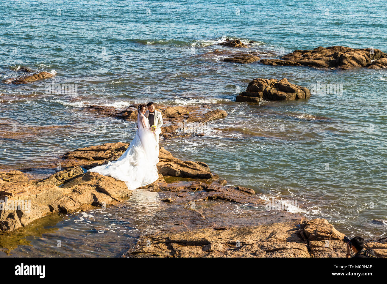 06-08-2016 - Qingdao, China - Chinese couple taking wedding albums photos among the rocks of Qingdao Coastline in Taiping Bay Stock Photo