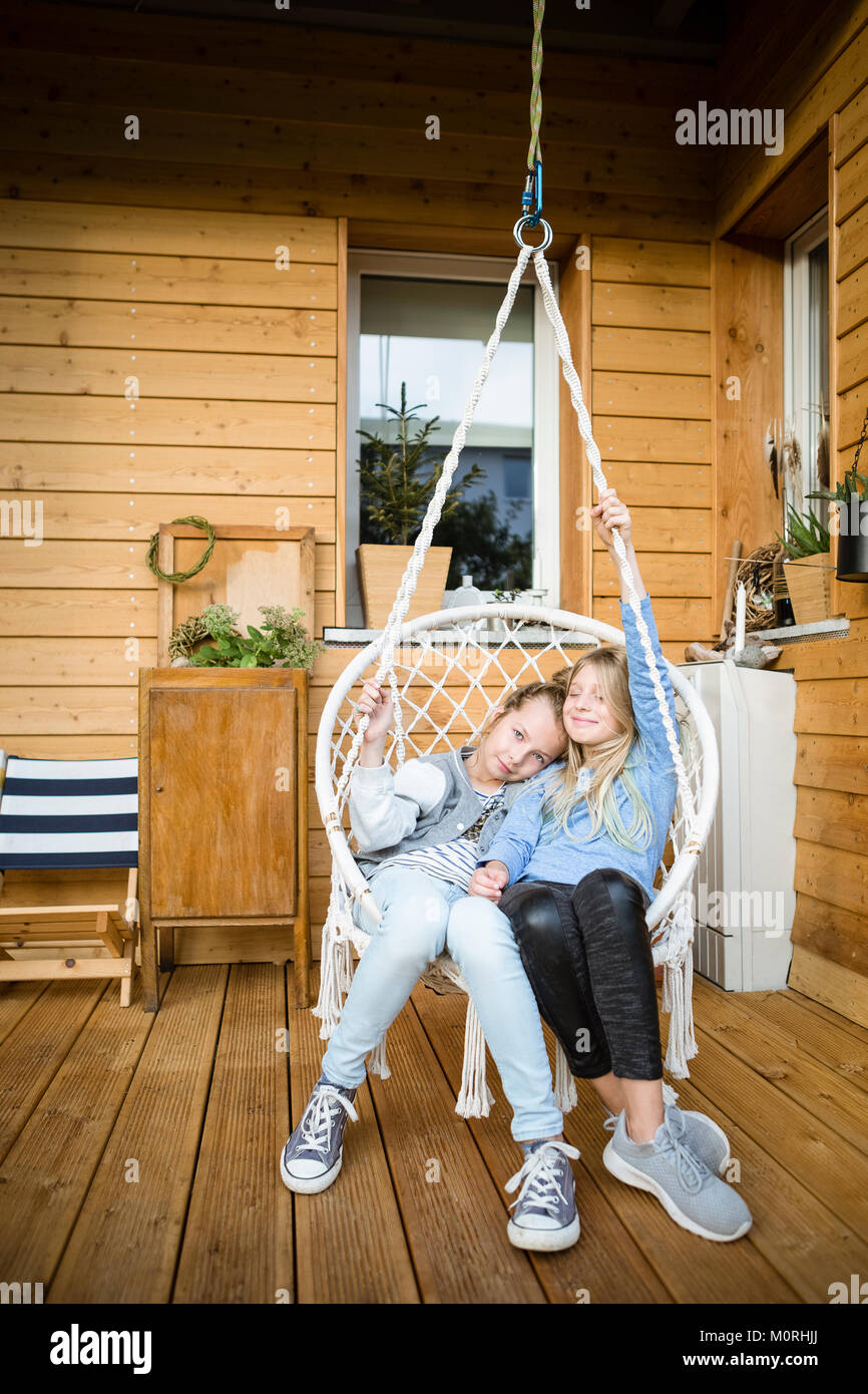 Two girls relaxing in a hanging chair on veranda Stock Photo