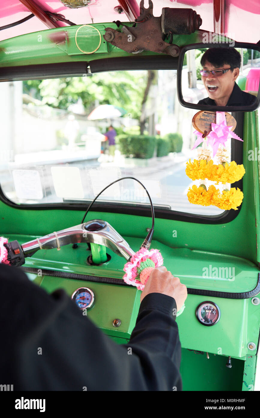 View from the mirror of a Tuk-tuk driver having fun with a traveler client traveling around Bangkok city, Thailand. Stock Photo
