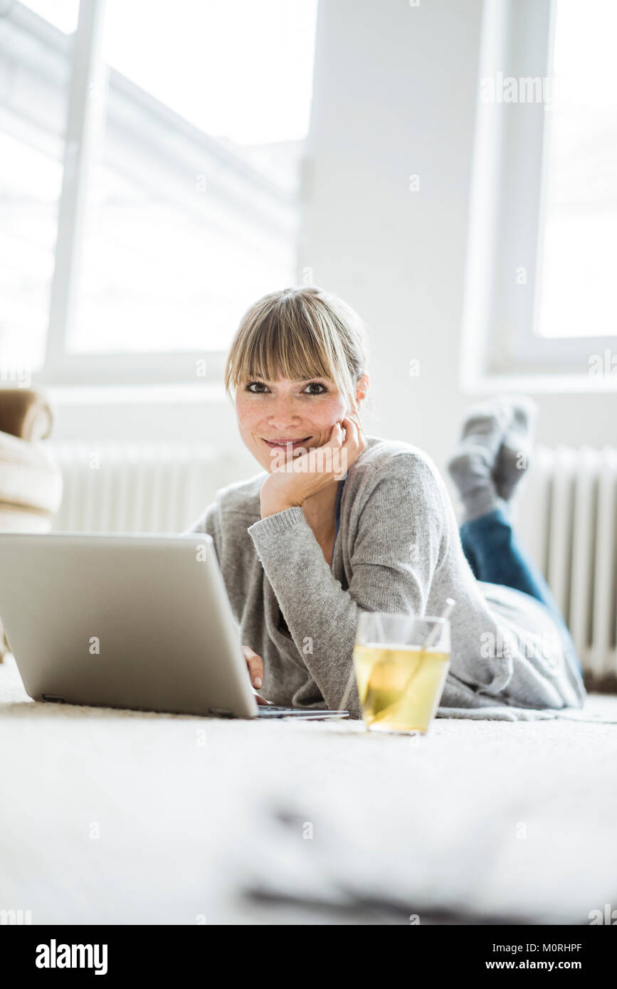 Smiling woman lying on the floor using laptop Stock Photo - Alamy